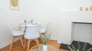 Zona pranzo con tavolo rotondo, sedie bianche e un vaso bianco con piante verdi.