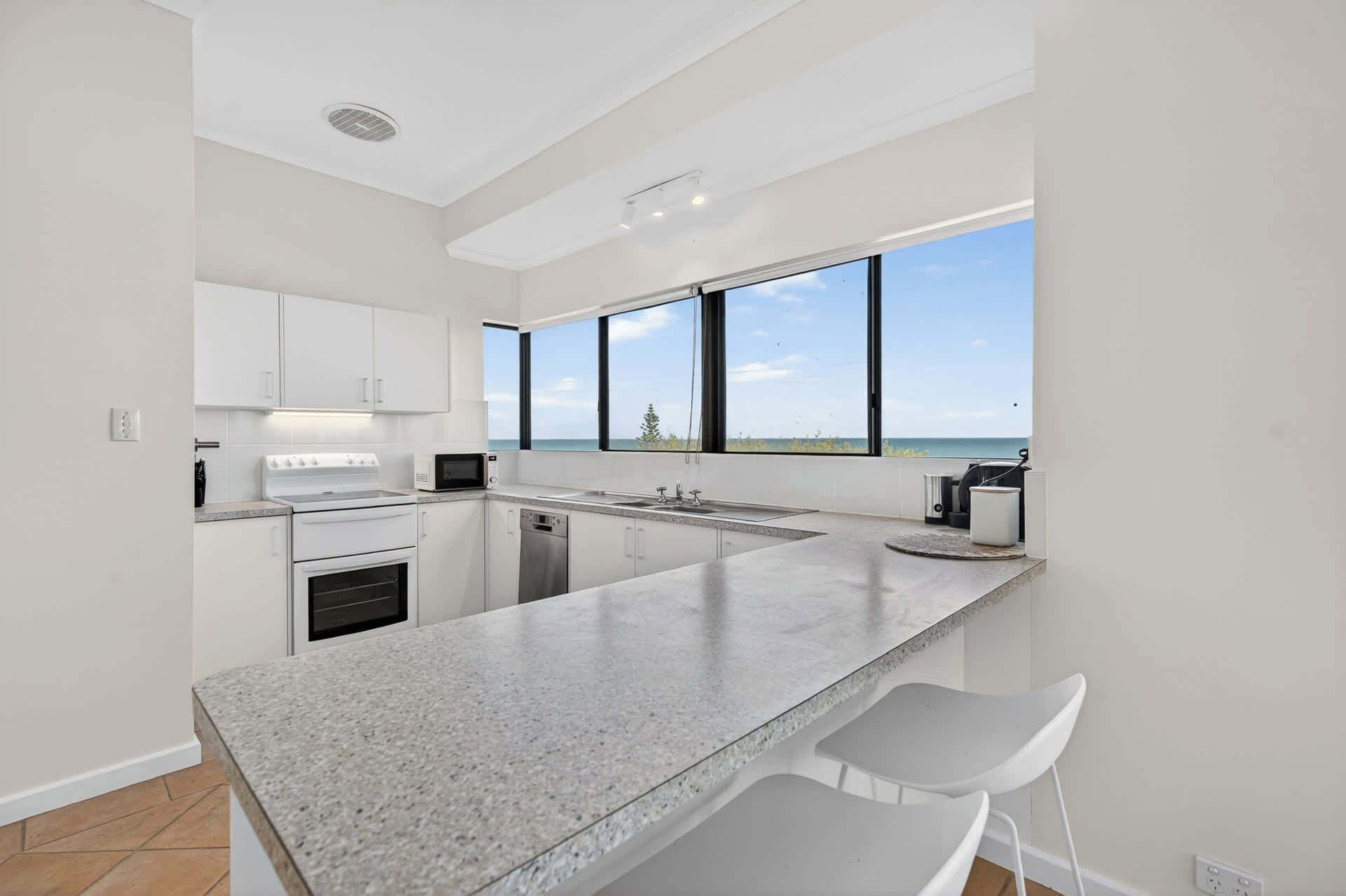 A modern kitchen with a large island, a view of the sea, and a high ceiling.