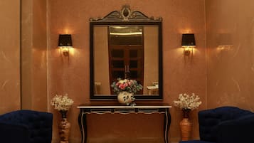 A lobby with a large mirror, two wall sconces, a console table with a vase of flowers, and two upholstered chairs.