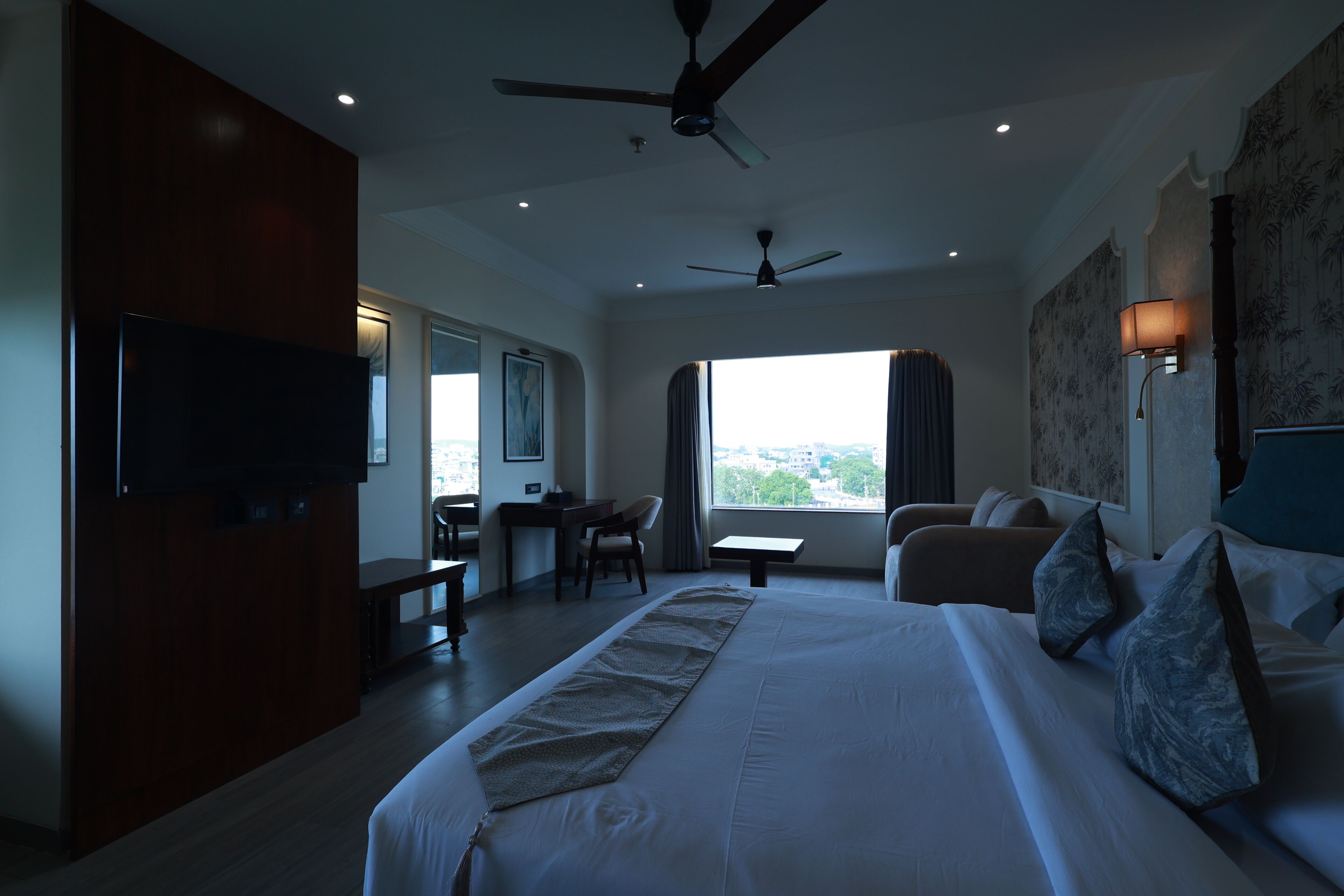 Una habitación de hotel con una cama grande, un escritorio, una silla, un televisor y un ventilador de techo.