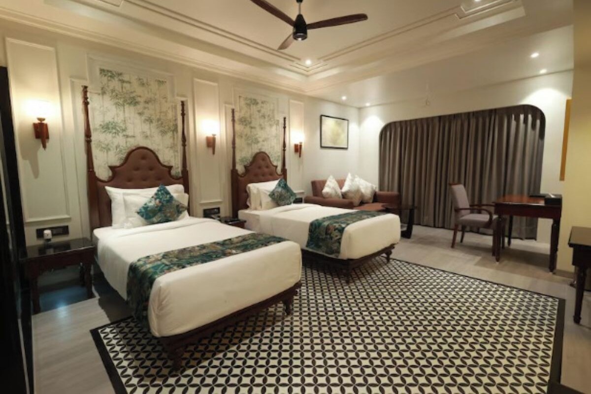 A hotel room with two beds, a ceiling fan, a patterned rug, and a desk with a chair.