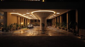 A hotel lobby with a central column, potted plants, and a parked car.