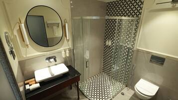 A bathroom with a round mirror, a sink, a toilet, and a glass-enclosed shower.