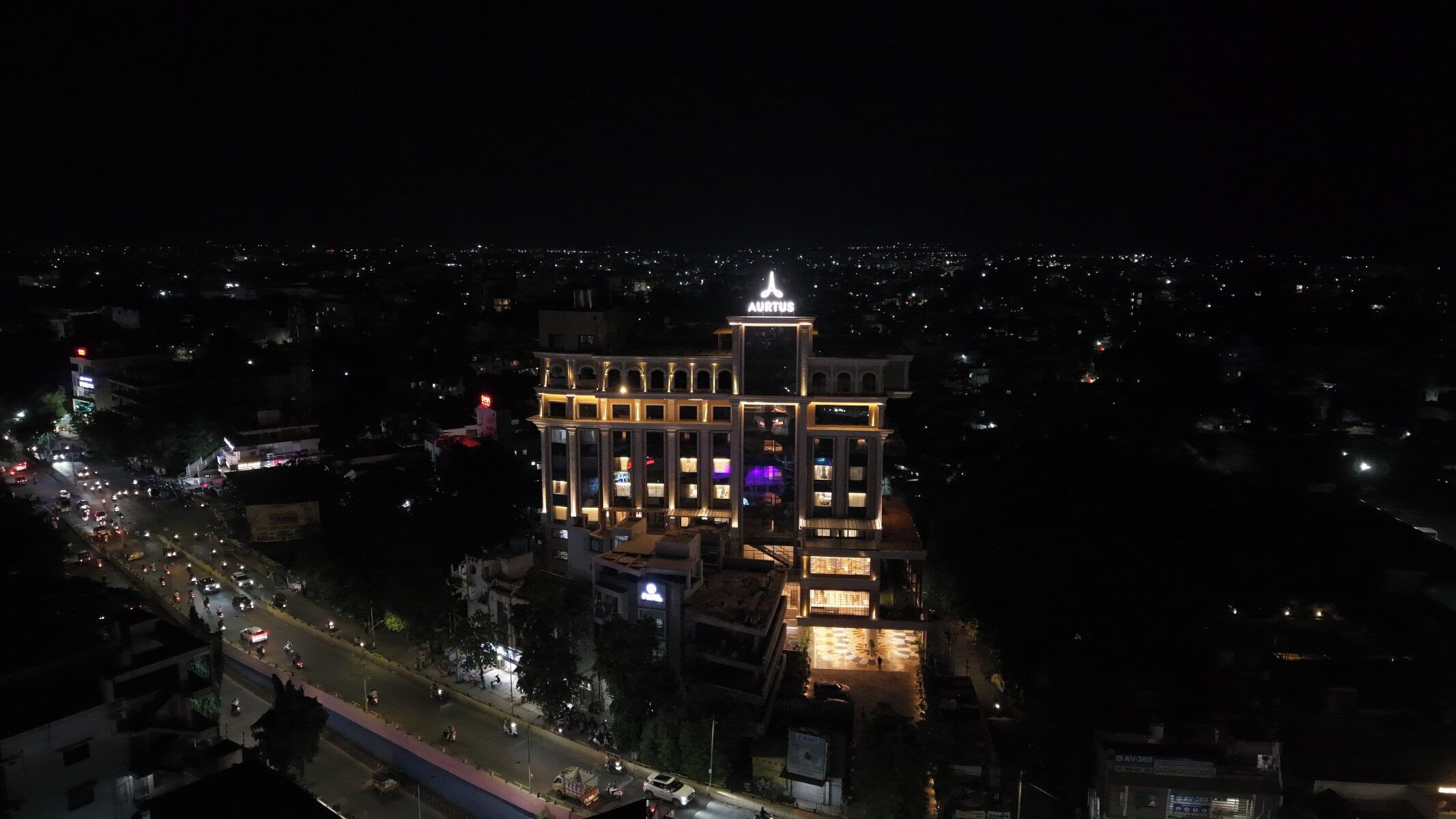 Un hôtel à plusieurs étages, doté d’une tour centrale imposante, de fenêtres illuminées et d’une entrée bien éclairée.