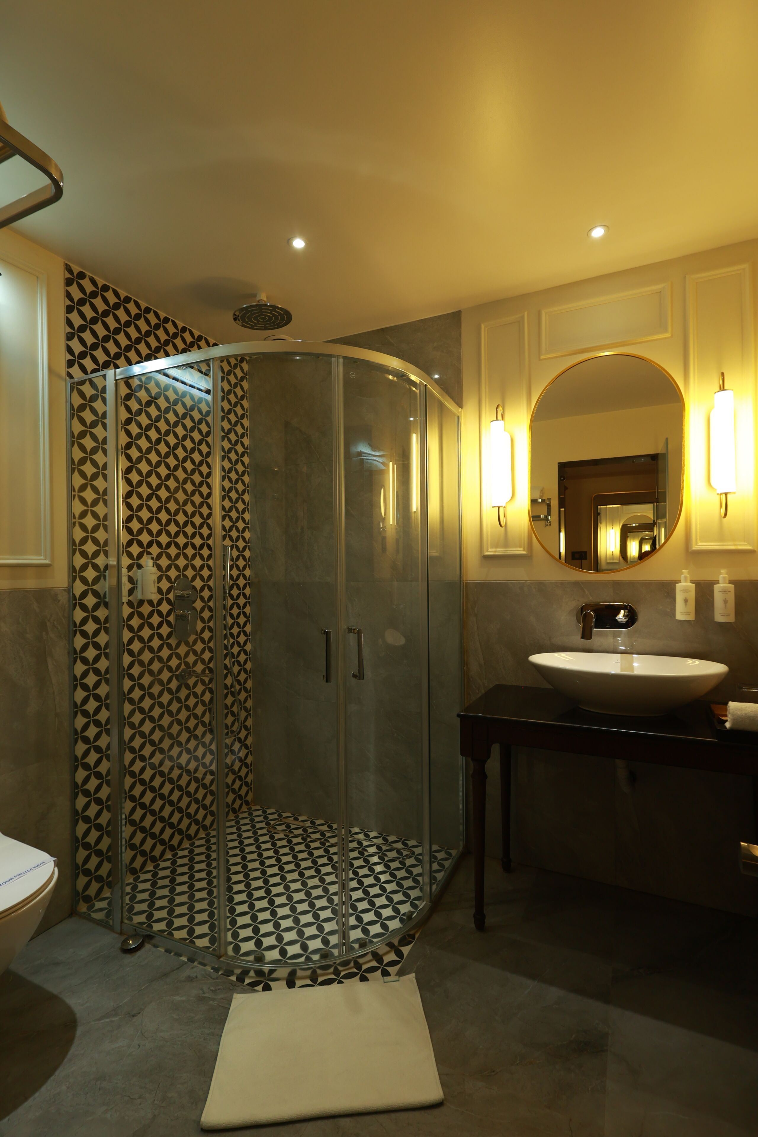 Een moderne badkamer met een douchecabine van glas, een ronde spiegel en een zwart wastafelmeubel met een witte wastafel.