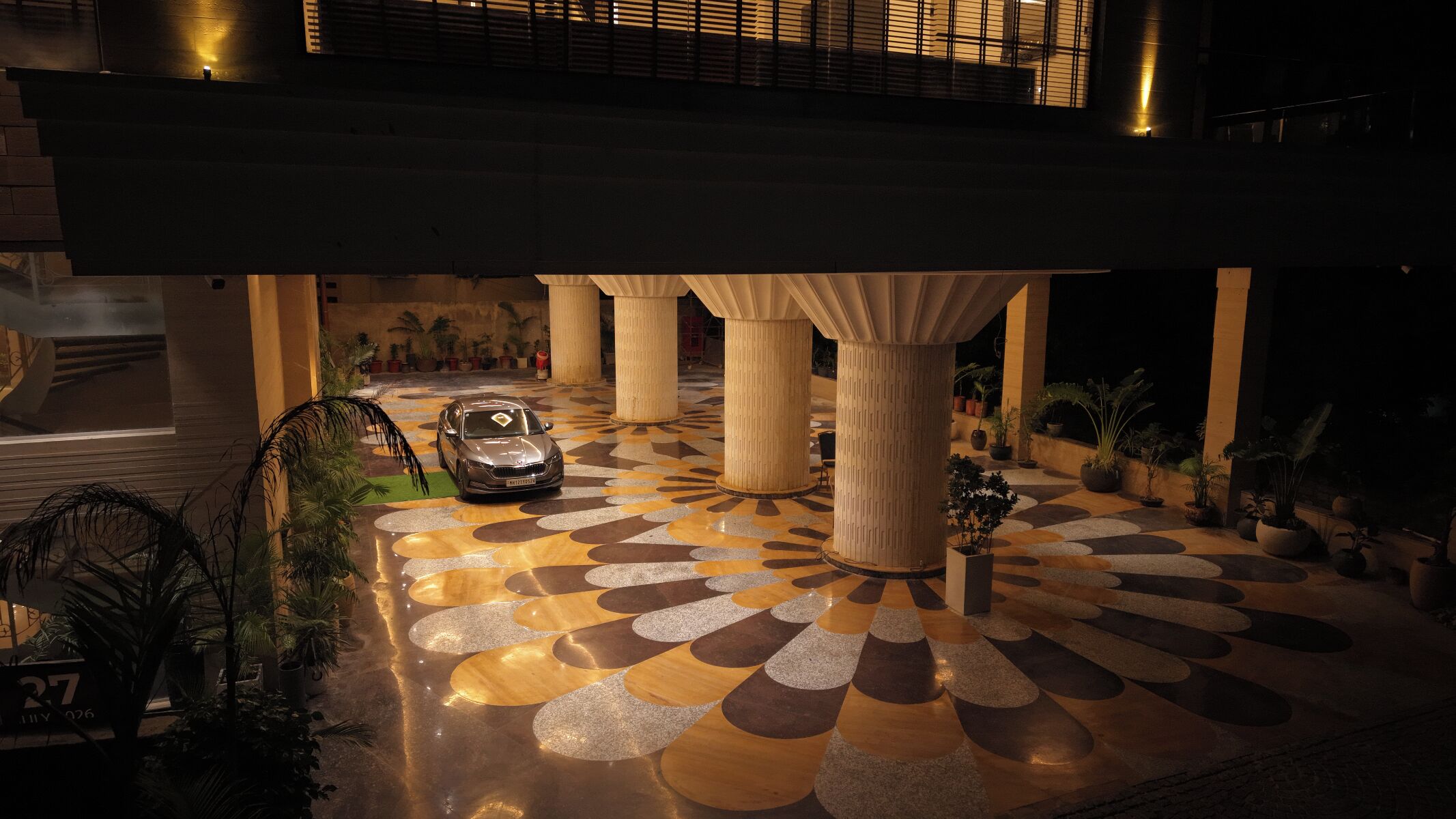 Un edificio moderno con un suelo de patrón geométrico, grandes columnas y un coche estacionado.
