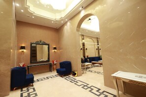 A hotel lobby with a marble floor, a large mirror, two blue armchairs, a small table, and a decorative console table. - Aurtus (Amravati)