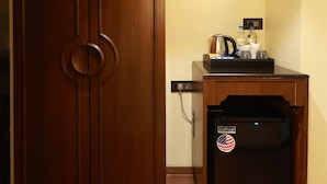 A room with a wooden wardrobe, a black refrigerator with a sticker, and a small table with a kettle and a bottle. - Aurtus (Amravati)