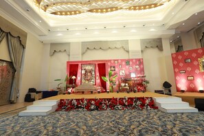A hotel room with a stage, red curtains, a patterned carpet, and a chandelier.
