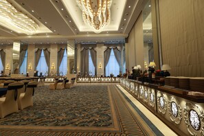 A hotel lobby with a long reception desk, seating area, and large windows with curtains.