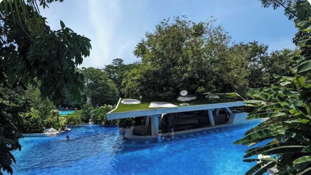 A pool with a floating bar area, surrounded by lush greenery.