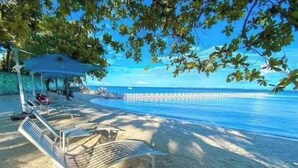 A beach with a lounge chair, a small shaded area, and a pier extending into the water.