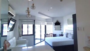 A modern bedroom with a large bed, a desk, and a large windows.