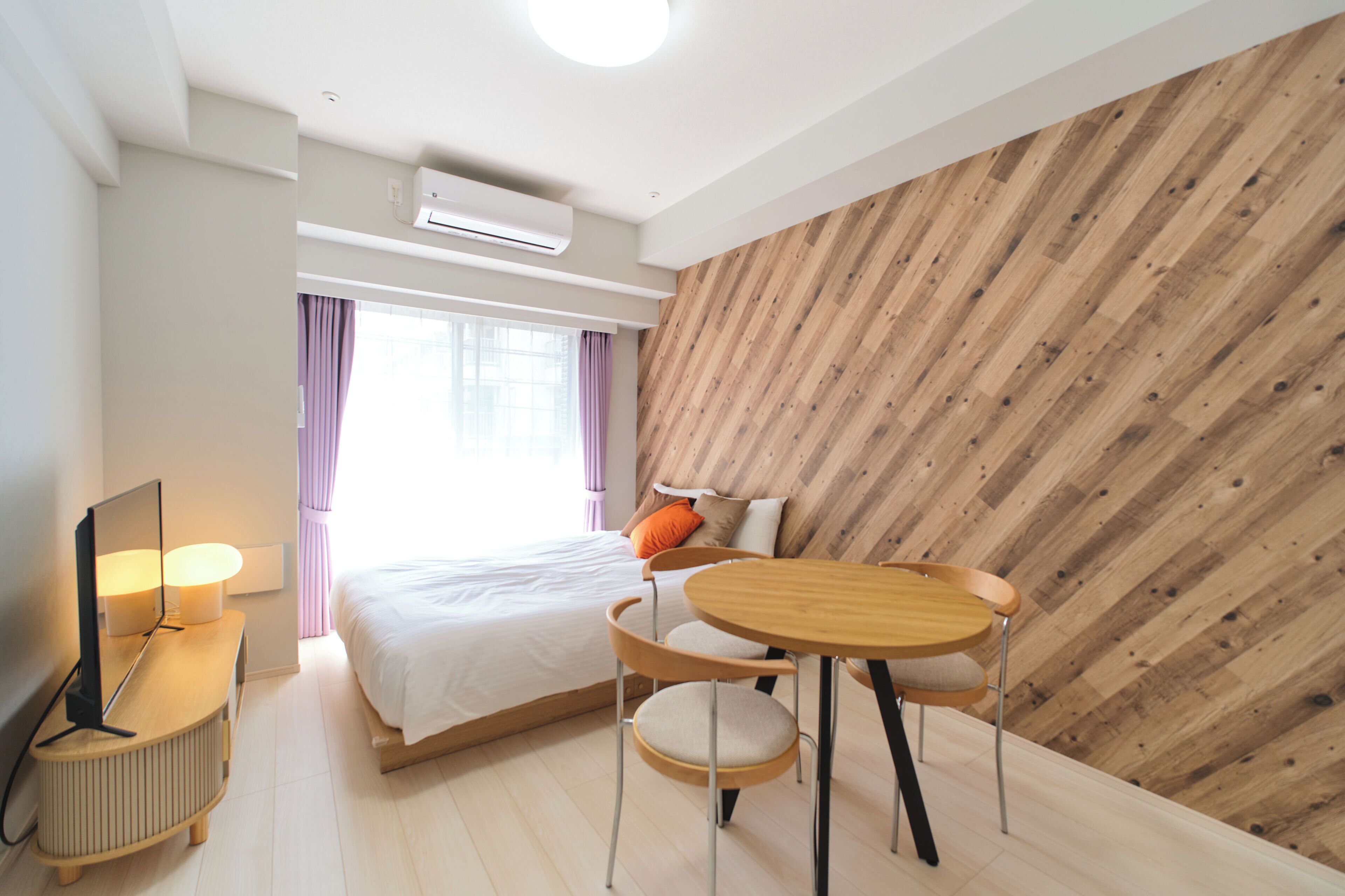 Una habitación de hotel moderna con una cama, una mesa redonda de madera, un televisor y un equipo de aire acondicionado.
