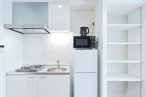 A modern kitchen with a gas stove, sink, microwave, and white cabinetry. - Sarcosuchus Higashikomagata (Tokyo)