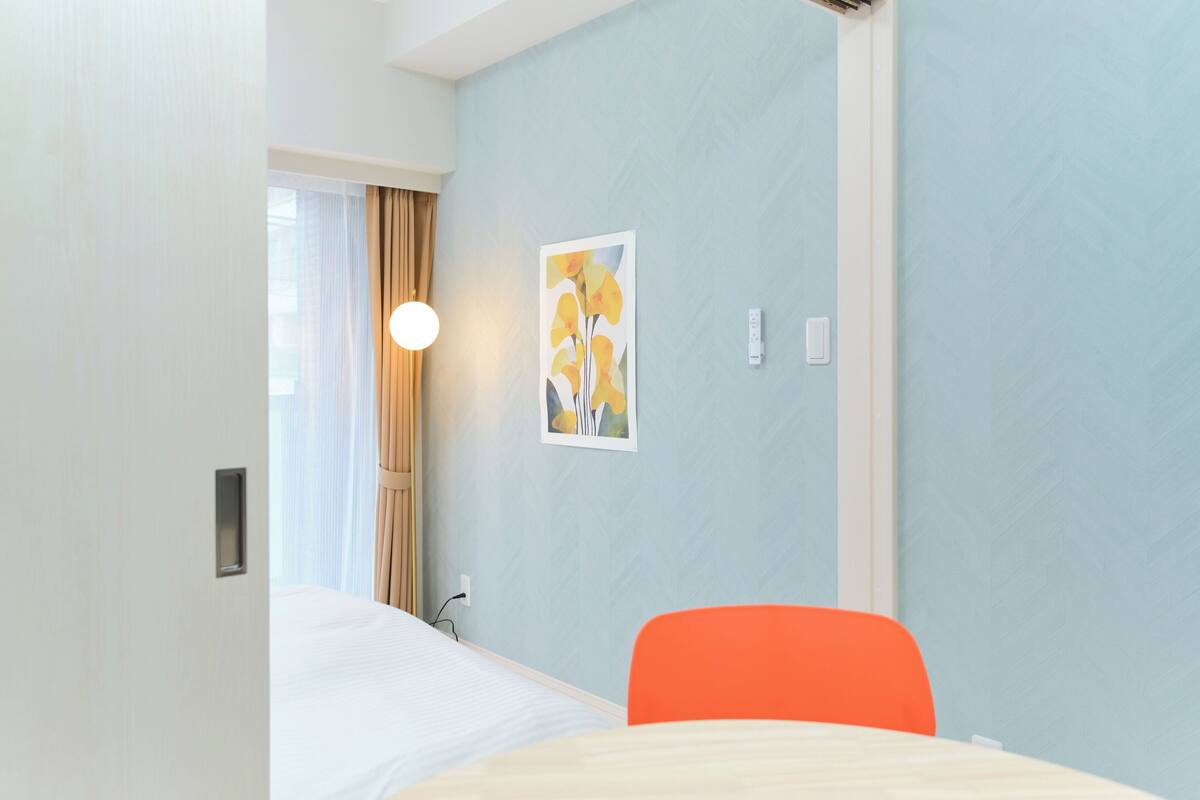 A hotel room with a bed, a chair, a wall-mounted light, and a painting.