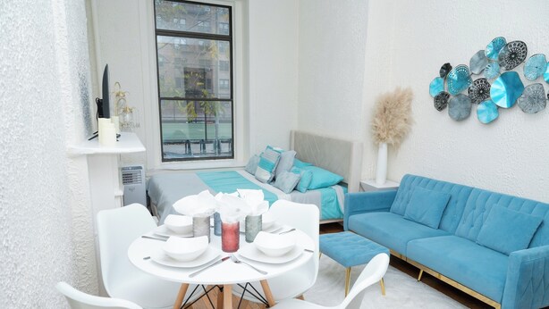 Un salon moderne avec un canapé bleu, des chaises blanches et une table à manger dressée pour quatre personnes.