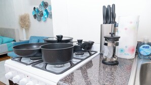 Une cuisine avec un fourneau blanc, trois casseroles noires, une machine à café et une bouteille de savon liquide.
