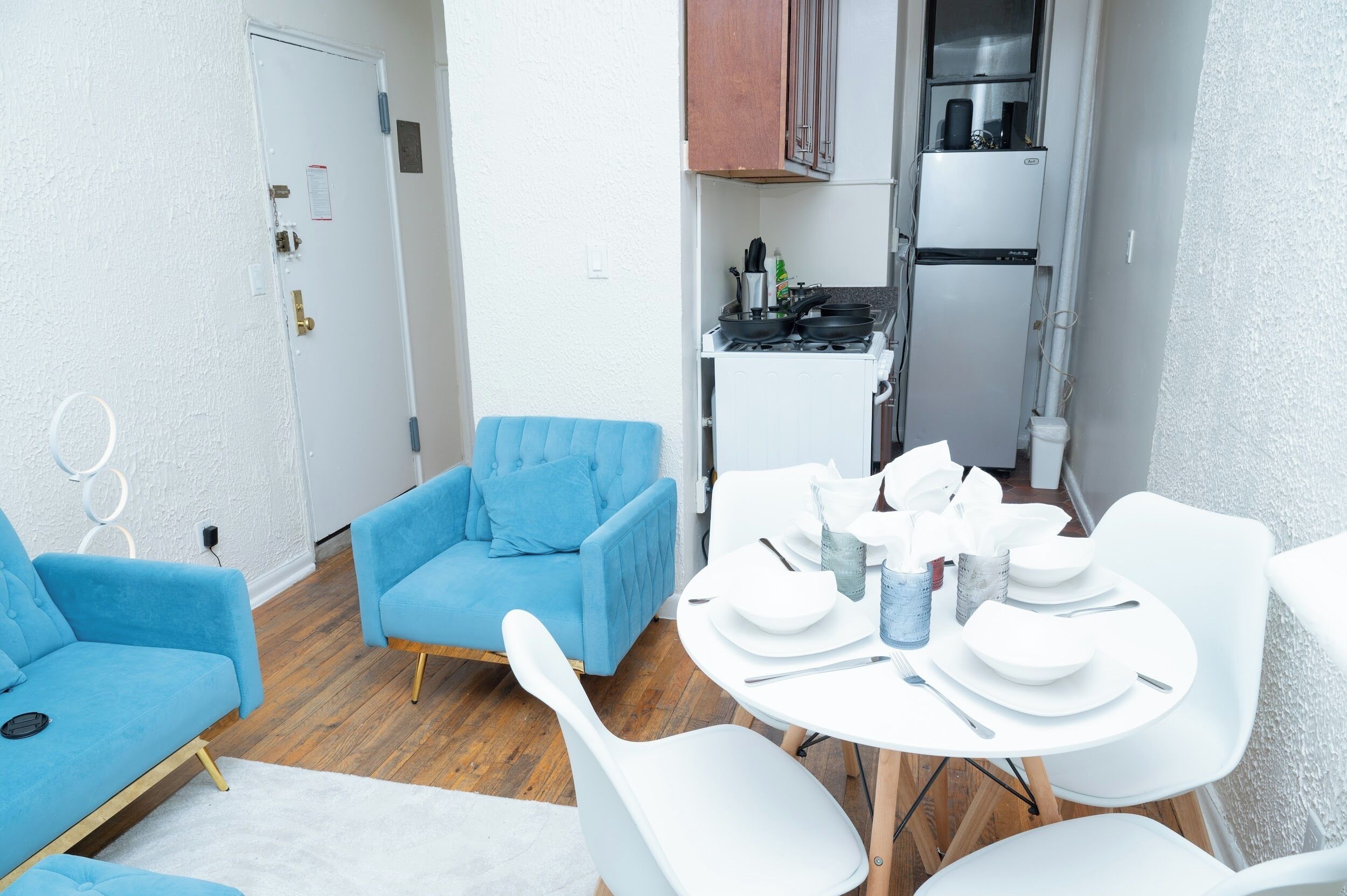 Una sala moderna con un sofá azul, una mesa de comedor para cuatro personas y una cocina con estufa y refrigerador.