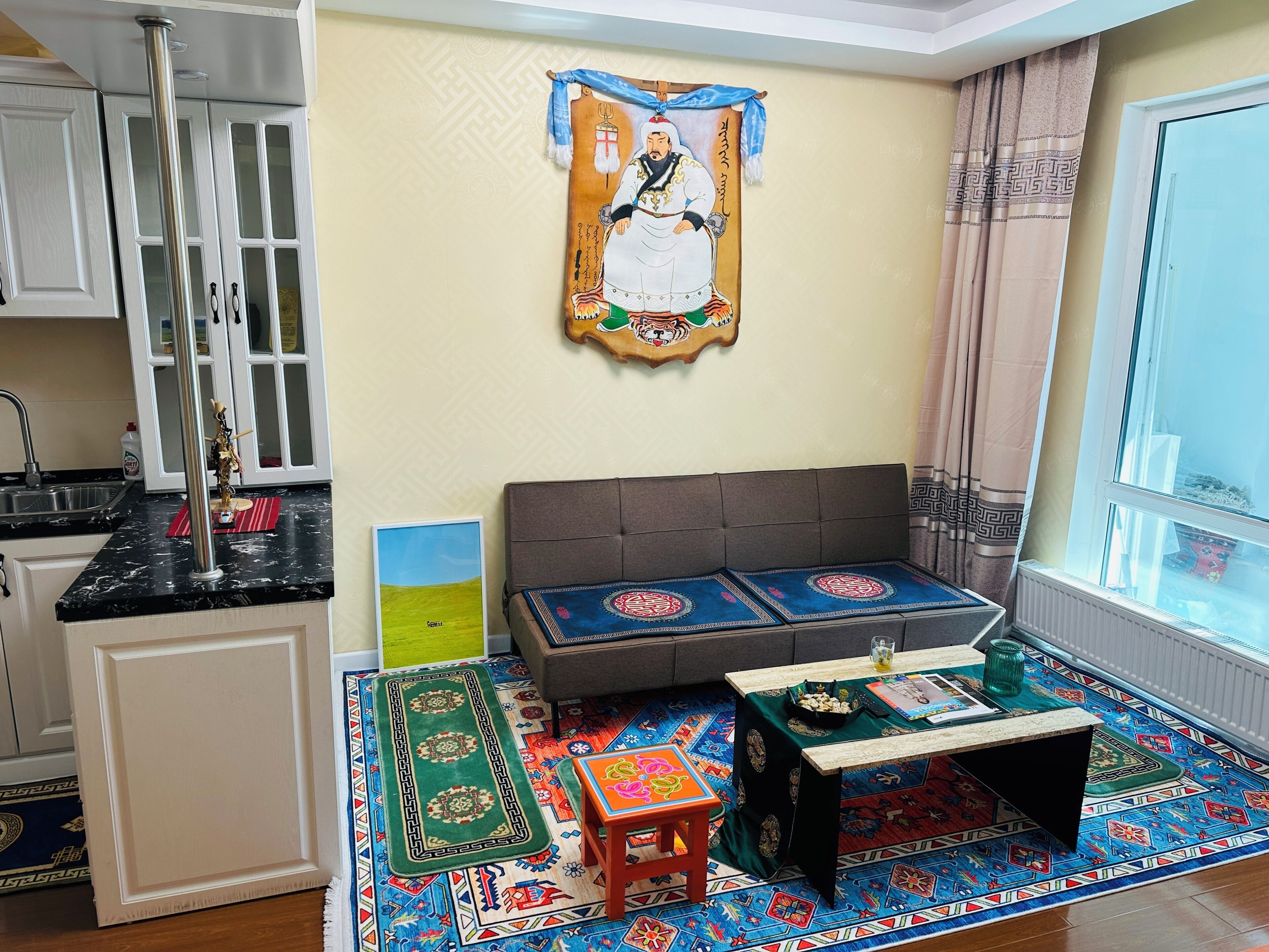 A compact living space with a kitchenette, a sofa set, a small table, and a colorful rug.