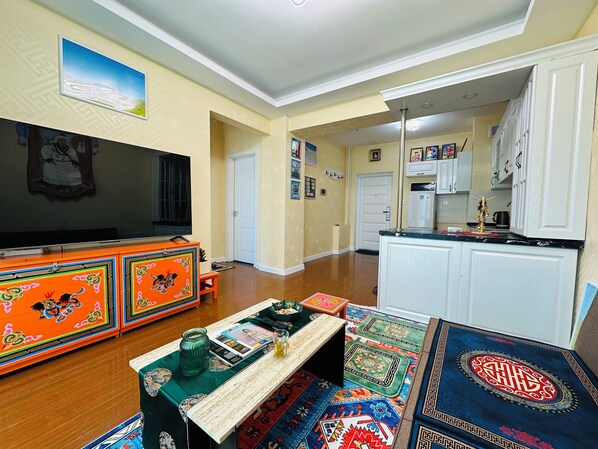 A living room with a TV, colorful cabinets, a coffee table with magazines, and a rug.