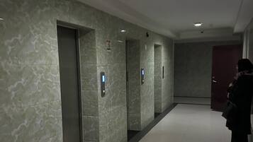 Un corridoio con ascensori, una porta rossa e una persona appoggiata al muro.