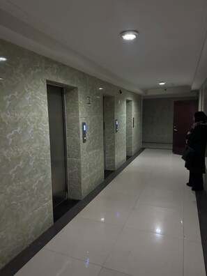 A hallway with elevators, a red door, and a person standing by the wall.