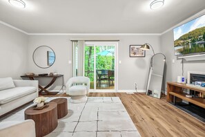 A modern living room with a white sofa, a round mirror, a wooden coffee table, and a large flat-screen TV.