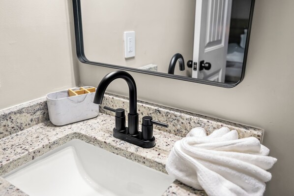 Un baño con lavamanos blanco, grifo negro y un perchero para toallas.