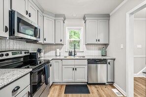 A modern kitchen with white cabinets, stainless steel appliances, and a window with blinds.