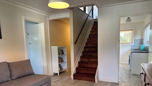 A living room with a sofa, a bookshelf, a staircase, and a kitchen area.
