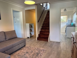 Una sala de estar con sofá, estantería, escalera y área de cocina.