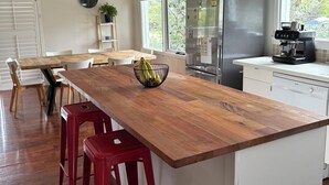 A kitchen with a wooden island, red bar stools, a refrigerator, a coffee machine, and a window with a view of trees.
