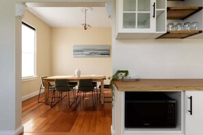 A dining area with a wooden table and chairs, a painting on the wall, and a microwave built into a cabinet. - Renovated Character Home with Modern Comforts (Invermay)