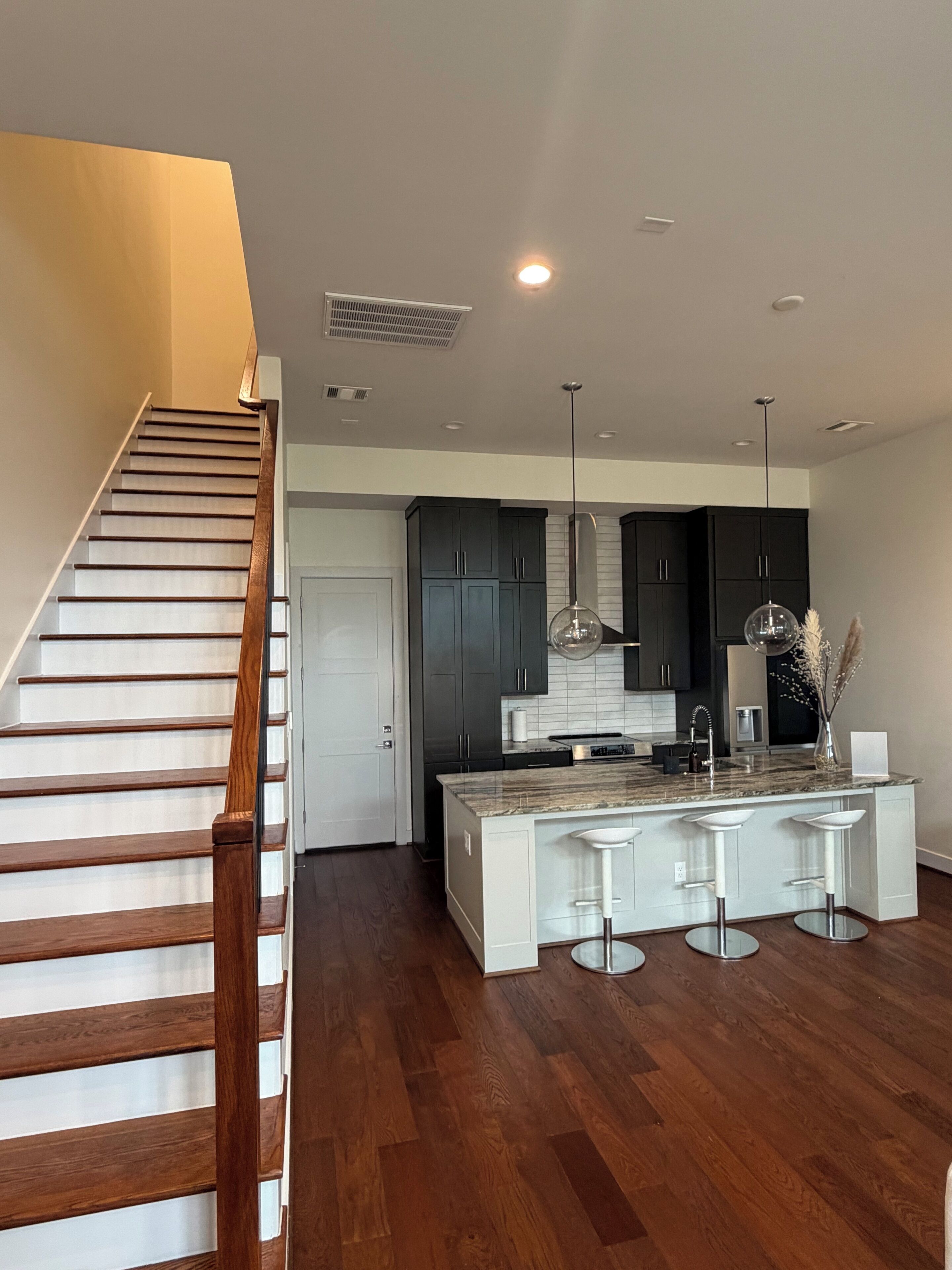 A modern kitchen with a central island, dark cabinets, and a wooden staircase. - 3Bed Sports Fan Oasis. 5 mins Astros, 10 mins NRG. (Houston)