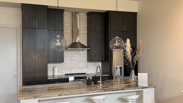 A modern kitchen with dark cabinets, a marble countertop, and a central island with bar stools. - 3Bed Sports Fan Oasis. 5 mins Astros, 10 mins NRG. (Houston)