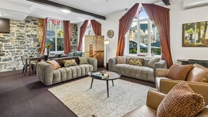 A living room with two sofas, a coffee table, a stone wall, and large windows with curtains.