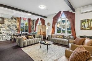 A living room with two sofas, a coffee table, a stone wall, and large windows with curtains. - Chapel On Moray (Dunedin)