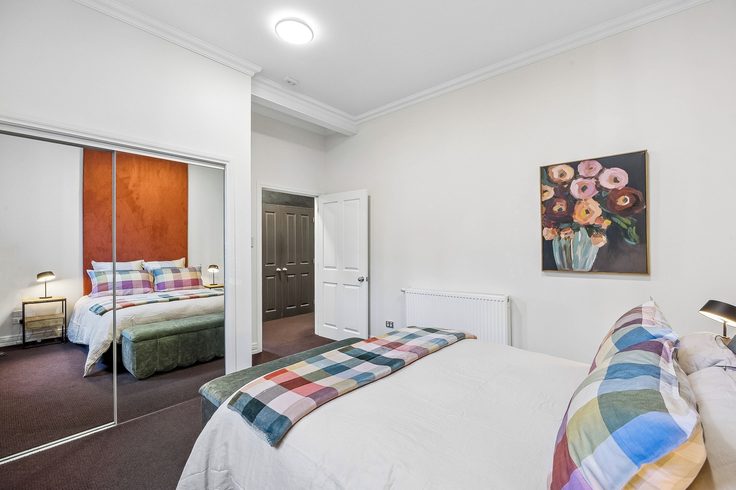 A bedroom with a large bed, a mirror, a radiator, and a painting on the wall.