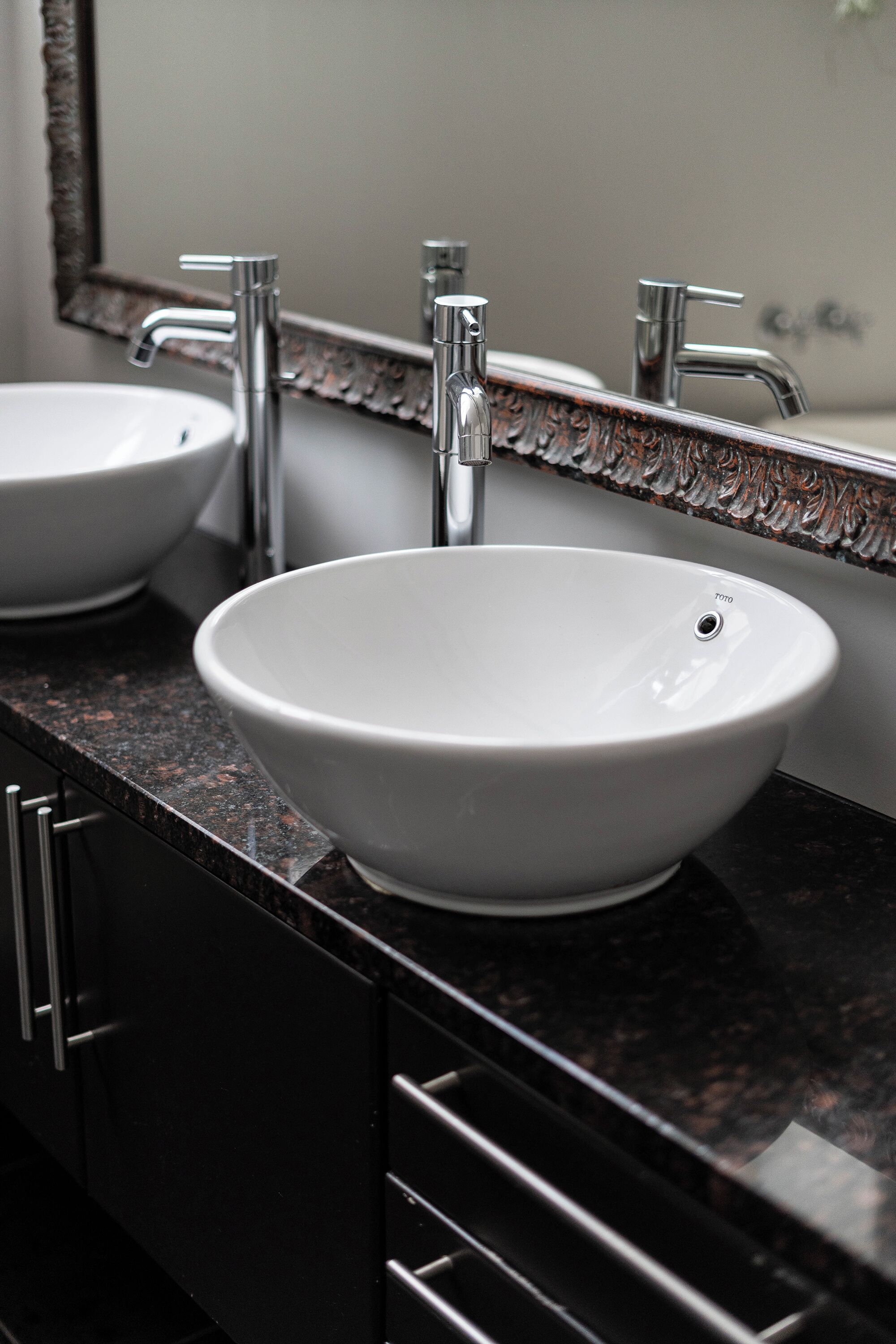 A bathroom with two white sinks, a mirror, and a dark granite countertop.