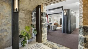 A stone-walled hallway with a potted plant, a metal light fixture, and a room with a sofa and a cabinet.