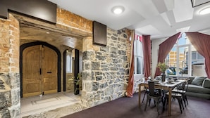 A stone wall, wooden door, dining table with chairs, and a sofa in a room with a view.