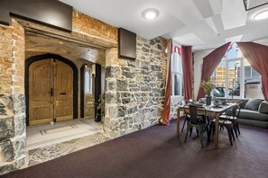 A stone wall, wooden door, dining table with chairs, and a sofa in a room with a view. - Chapel On Moray (Dunedin)
