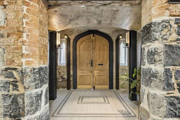 A stone-walled hallway with a wooden door, a tiled floor, and a potted plant. - Chapel On Moray (Dunedin)