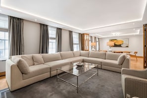A modern living room with a large L-shaped sofa, a glass coffee table, and a dining area with a wooden table and chairs. - Mayfair 3-bed With Central AC Upper Grosvenor St (London)