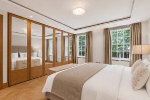 A bedroom with a large bed, a wardrobe, a bedside table, and a window with curtains. - Mayfair 3-bed With Central AC Upper Grosvenor St (London)