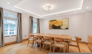 Ein Essbereich mit einem Holztisch und Stühlen, einem Bild an der Wand und einem Fenster mit Vorhängen.