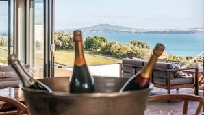A room with a view of the sea, a bucket with bottles, and a chair. - Tradewinds Retreat by Waiheke Pure - Views views views, pool, spa, luxurious spacious living (Waiheke Island)