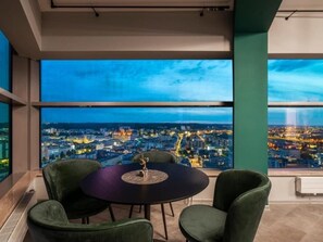Ein Zimmer mit großem Fenster und Blick auf eine beleuchtete Stadtlandschaft bei Nacht.