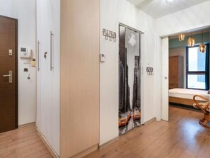 Ein Flur mit Holzboden, einer Tür mit Schlüsselsperre, einem an der Wand befestigten Lichtschalter und einem Fenster mit Blick auf Gebäude.